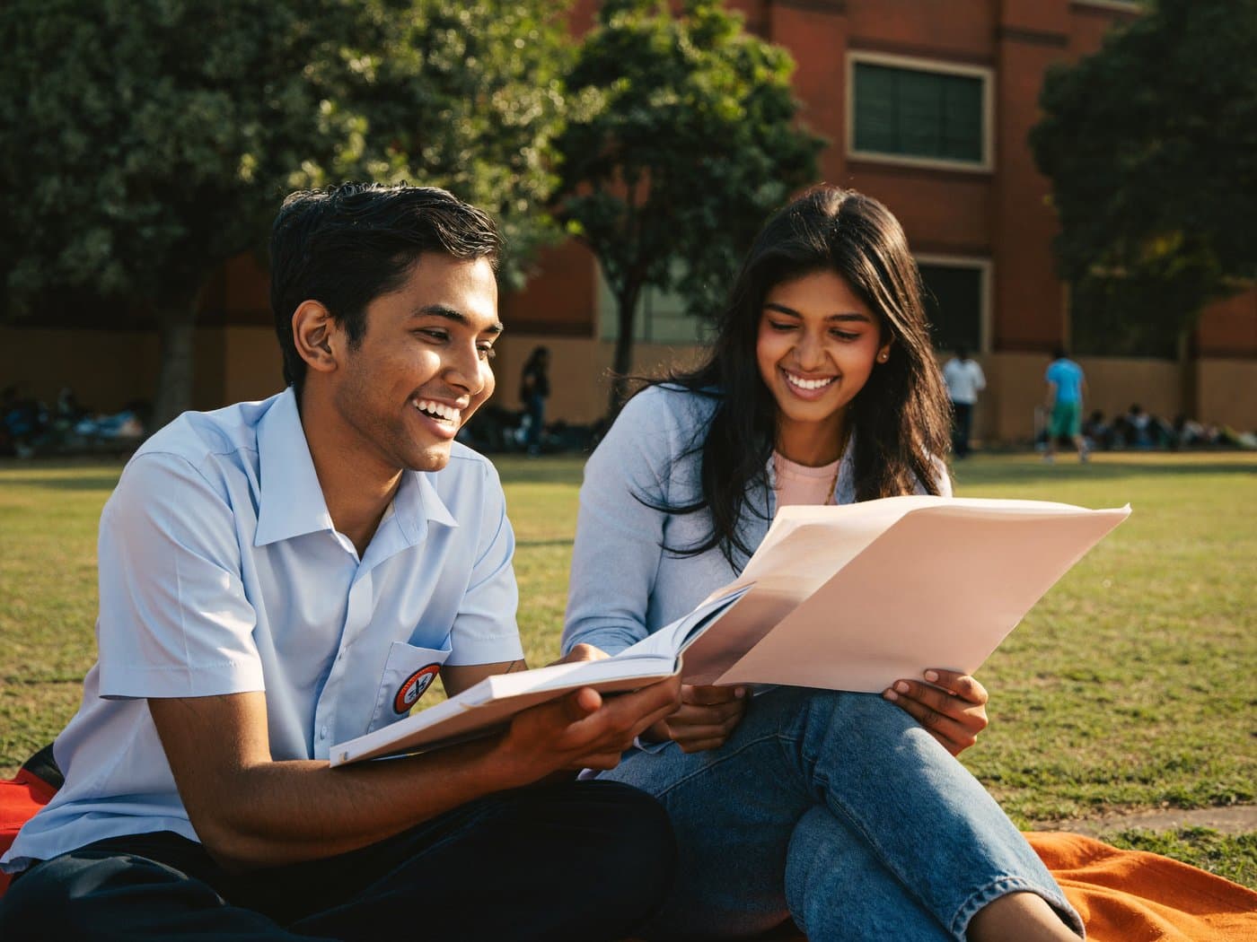 Two Indian students studying together outdoors on a campus lawn